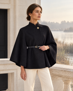 Maison Aue margaux stand collar cape in Black, editorial model pose at limestone pavilion