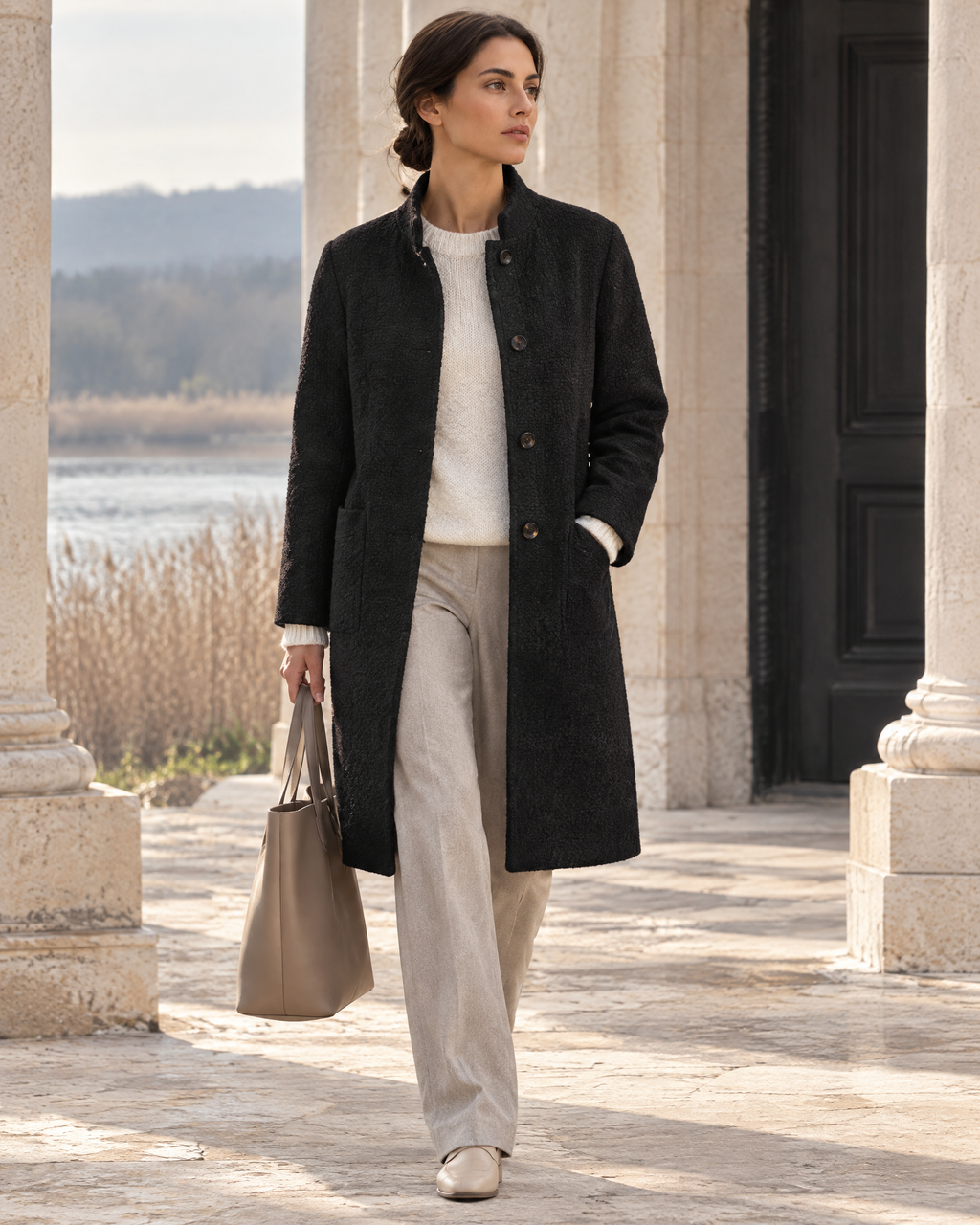 Maison Aue sabine stand collar coat in Black, editorial model pose at limestone pavilion